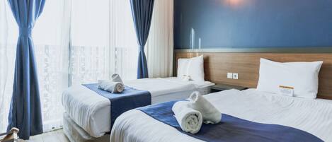 Una habitación de hotel con dos camas, un cabecero de madera, una mesita de noche y una ventana con cortinas.