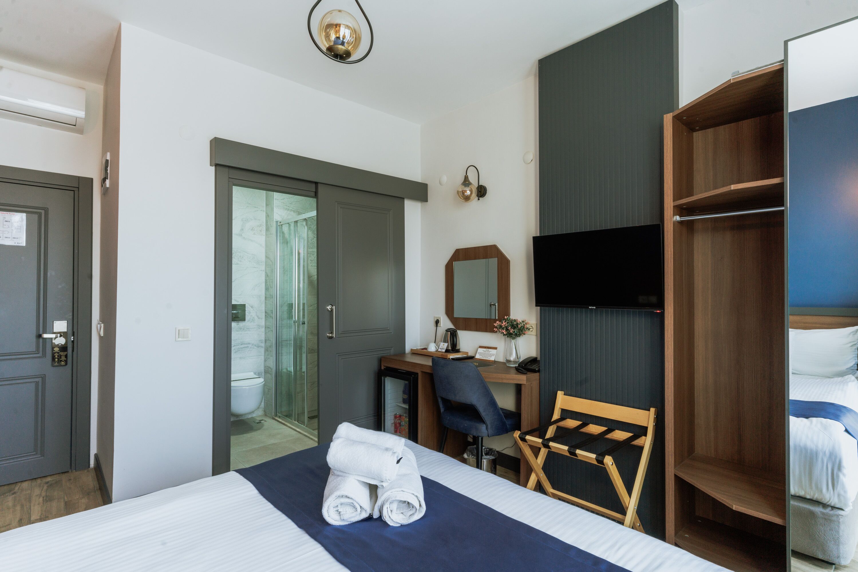 A hotel room with a bed, a desk, a chair, a wardrobe, and a television.