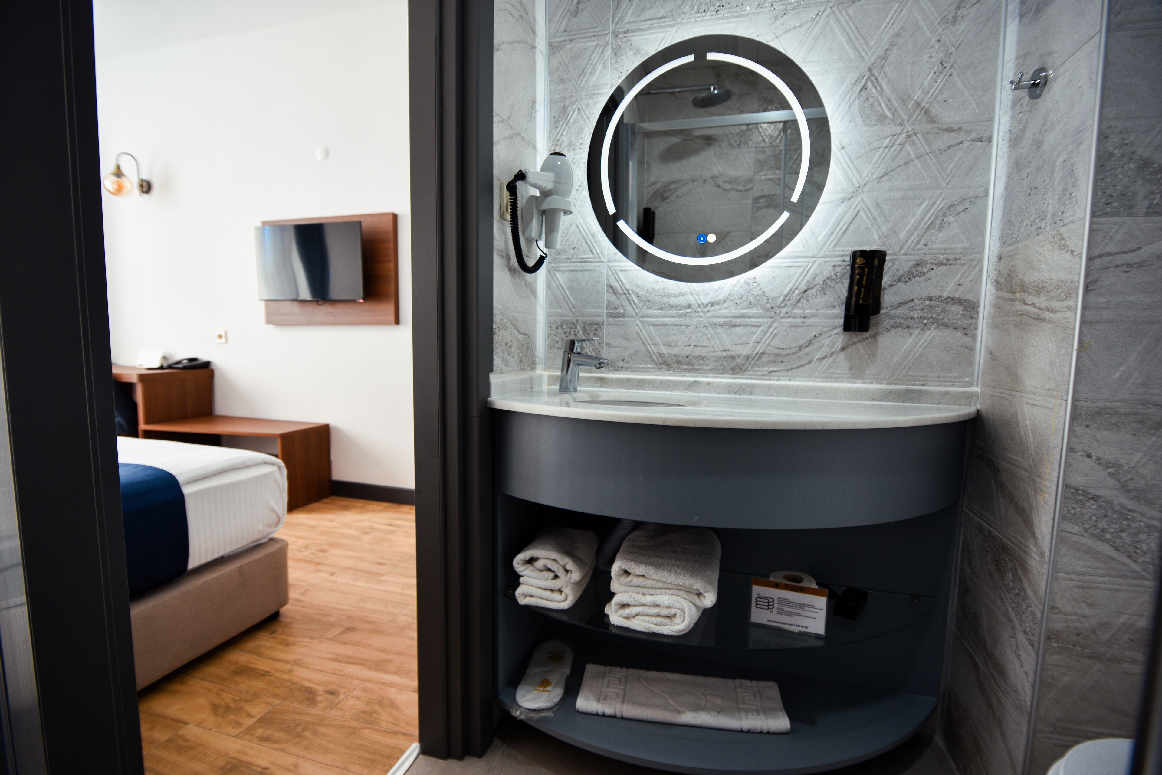 A modern bathroom with a round mirror, built-in sink, and a shelf with folded towels.