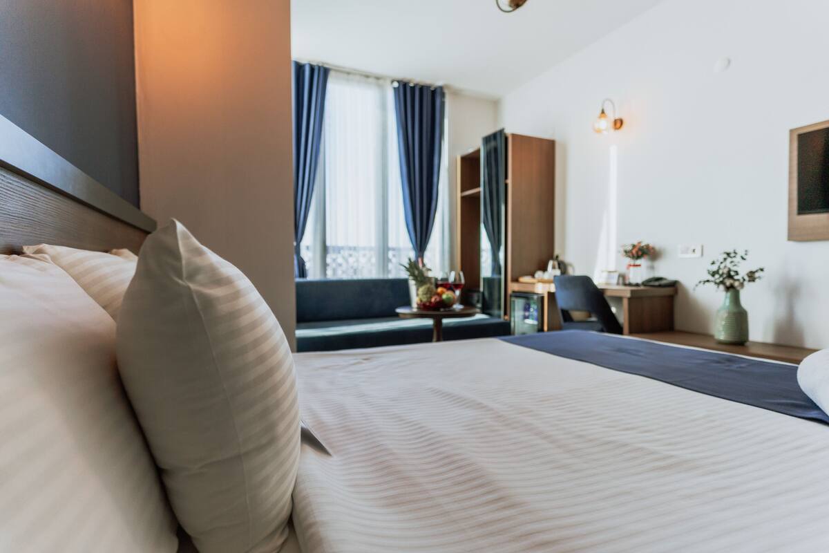 Una habitación de hotel con una cama, un escritorio, una silla, un sofá y una ventana con cortinas.