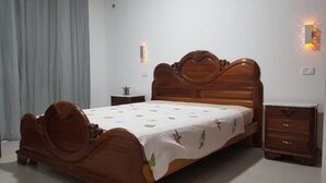 A wooden bed with a floral bedspread, a nightstand, a dresser, and wall sconces.