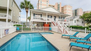 A pool area with two pools, white fences, and blue lounge chairs.