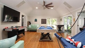 A spacious room with a pool table, a sofa, a television, and a ceiling fan.