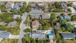 An aerial view of a residential area with houses, a swimming pool, and a beach in the background.