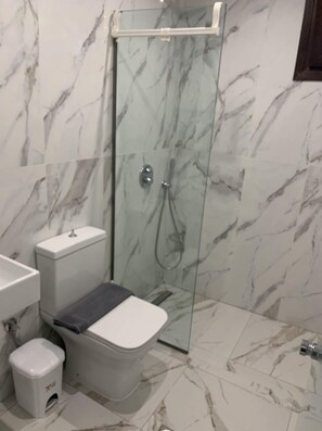 A bathroom with a glass-enclosed shower, a white toilet, and a small trash bin.