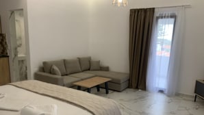Habitación de hotel con cama, sofá, una mesa de centro y vistas al exterior a través de una ventana.