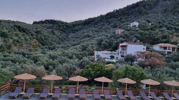 Zona de piscina con sillones reclinables y sombrillas, rodeada de un paisaje montañoso.