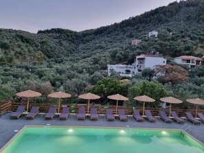 A pool area with lounge chairs and umbrellas, surrounded by a mountainous landscape.