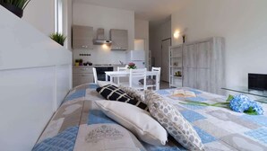 A modern, compact living space with a kitchenette, dining area, and a bed with patterned bedding. - Casetta di Elie - Affitti Brevi Italia (Lecco)