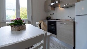 A modern kitchen with a white table, a stove, an oven, and a refrigerator. - Casetta di Elie - Affitti Brevi Italia (Lecco)