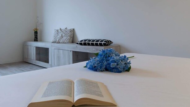 Een keurig opgemaakt slaapkamer met een bed, een open boek en een bloevas.