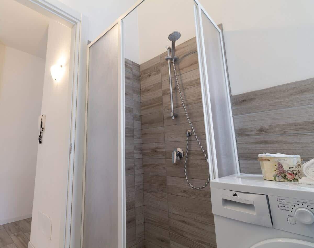 A bathroom with a walk-in shower, a white washing machine, and a towel dispenser.