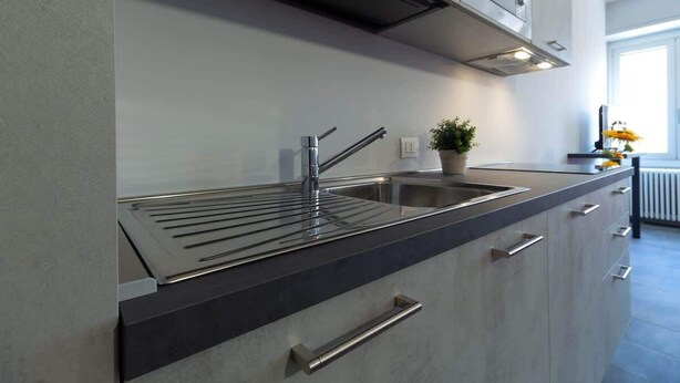 Een moderne keuken met een roestvrijstalen spoelbak, een zwart aanrecht en lichtgekleurde kastjes.
