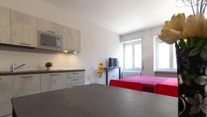 Een moderne keuken met grijze kastjes, een magnetron en een eethoek met een rode tafel.