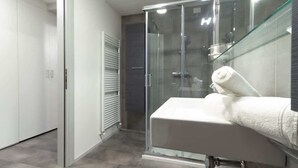 Een moderne badkamer met een douchecabine van glas, een wit wastafelmeubel met een handdoek, en een betegelde vloer.