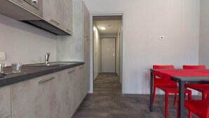 A modern kitchen with grey cabinets, a black countertop, and a red dining table with matching chairs. - Appartamento Papavero - Affitti Brevi Italia (Lecco)