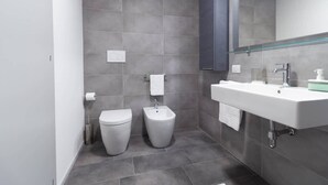 A modern bathroom with a toilet, bidet, and a large sink with a mirror above. - Appartamento Papavero - Affitti Brevi Italia (Lecco)