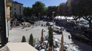 A view from a balcony overlooking a street with parked cars, a parking lot, and a building with multiple floors. - Lungolago Holiday Home - Affitti Brevi Italia (Lecco)