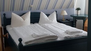Een netjes opgemaakt bed met witte lakens, een donker hoofdbord en een nachtkastje met een lamp.