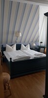 Uma cama bem arrumada com lençóis brancos, cabeceira escura e mesa de cabeceira com abajur.
