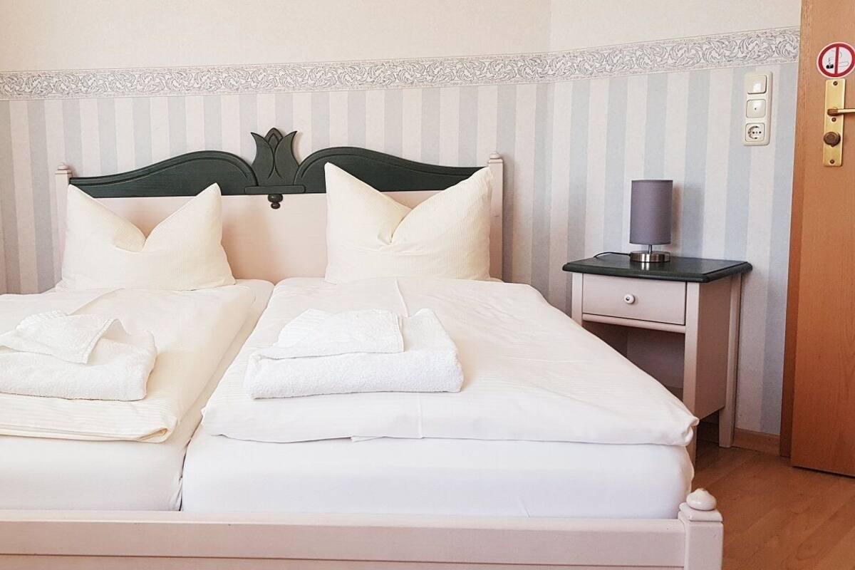 Un lit double avec du linge de lit et des serviettes blanches, deux tables de chevet avec des lampes, une tête de lit décorative et un mur à rayures.