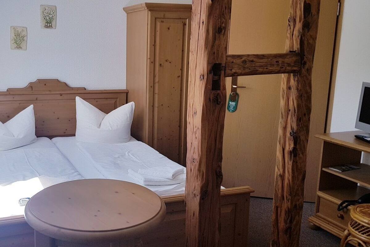 Une chambre à coucher avec un lit en bois, une table de chevet avec une lampe, une petite table ronde et une armoire en bois.