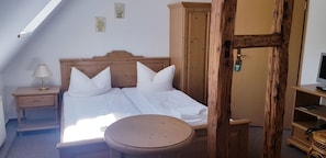 Un dormitorio con una cama de madera, una mesita de noche con lámpara, una pequeña mesa redonda y un armario de madera.