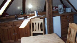 Een kleine keuken met houten kastjes, een houten eettafel en stoelen. Er is een spoelbak, een koffiezetapparaat en een broodrooster op het aanrecht.