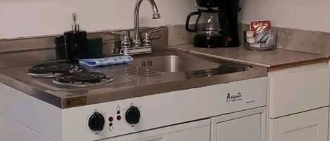 A compact kitchen with a stove, sink, and coffee maker.