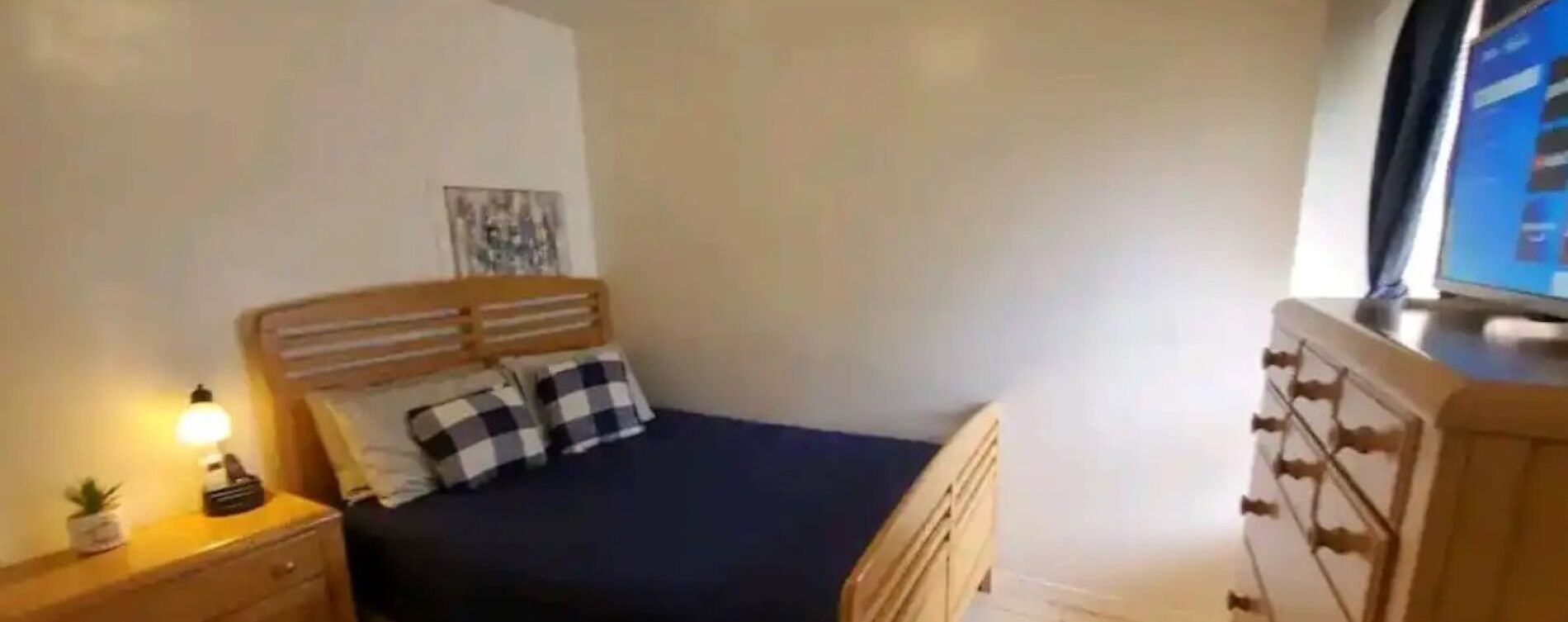 A bedroom with a bed, a bedside table with a lamp, a dresser, and a window.