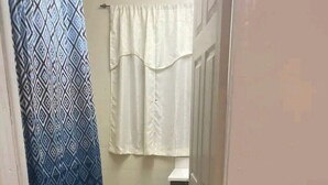 A narrow bathroom with a patterned shower curtain, a white towel hanging, and a blue mat on the floor. - #20 Marjory’s in-law suite (Tampa)