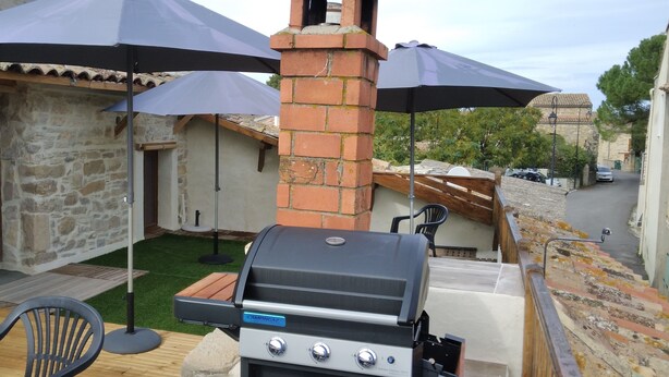 Eine Terrasse mit Grill, Steinmauern und Sonnenschirmen, die Schatten spenden.