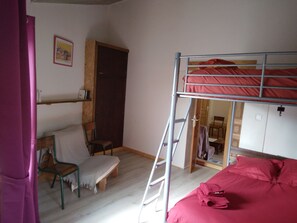 A dormitory room with bunk beds, a desk, a chair, and a wooden door.