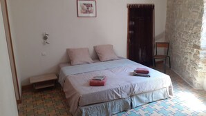 Ein Schlafzimmer mit Bett, Kissen, einer kleinen Bank, einem Bild an der Wand und einer Steinwand.