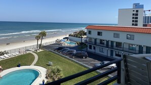 Vista de un hotel frente a la playa con piscina, estacionamiento y vista al océano.