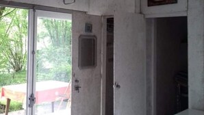 Una habitación con un ventanal grande, una puerta que da al exterior, un ventanuilla pequeña y una estufa.