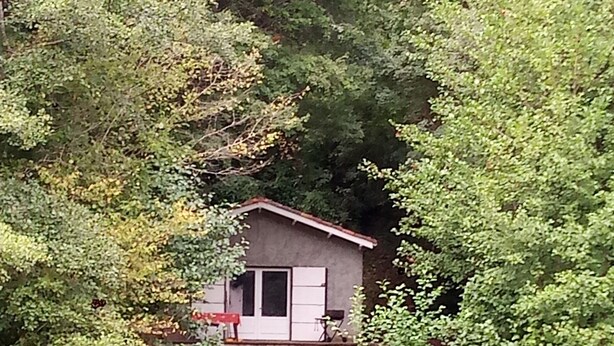 Una cabaña pequeña y rústica con cimientos de piedra, una terraza de madera y una sola puerta.