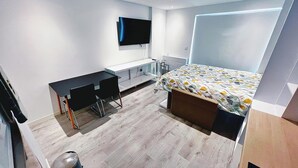 A modern hotel room with a bed, a desk, a chair, a TV, and a radiator. - Modern Studio Apartment Gibraltar (Gibraltar)