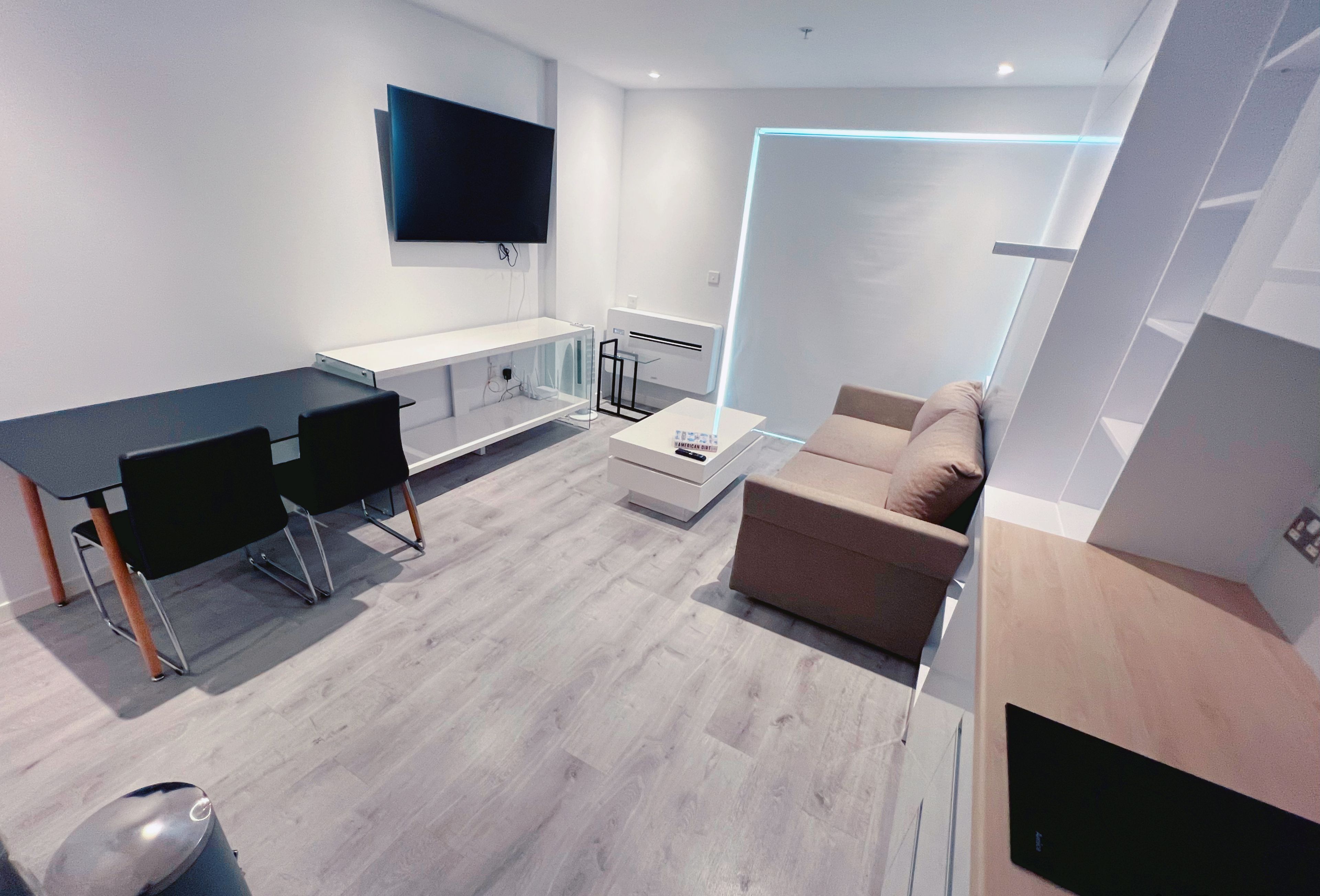 Een moderne woonkamer met een eethoek, een flatscreen tv aan de muur, een bank en een salontafel.