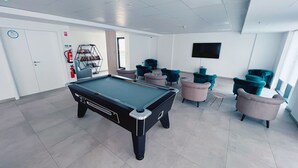 A pool table in a modern room with teal and pink chairs, a bookshelf, and a fire extinguisher. - Modern Studio Apartment Gibraltar (Gibraltar)