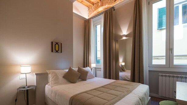 Un dormitorio ordenado con cama, lámpara de noche y vistas al exterior a través de una ventana.