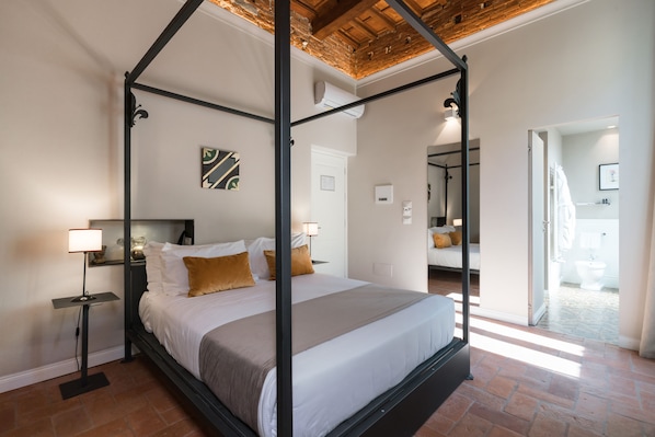 A four-poster bed with a modern design, a nightstand with a lamp, and a view of the bathroom through an open door. - Atelier delle Grazie (Florence)