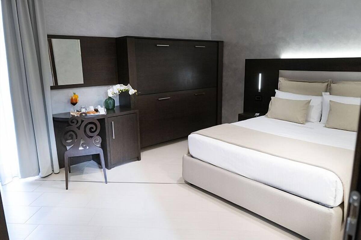 Une chambre moderne avec un grand lit, une armoire en bois foncé, un petit bureau avec une chaise et une table de chevet avec une lampe.