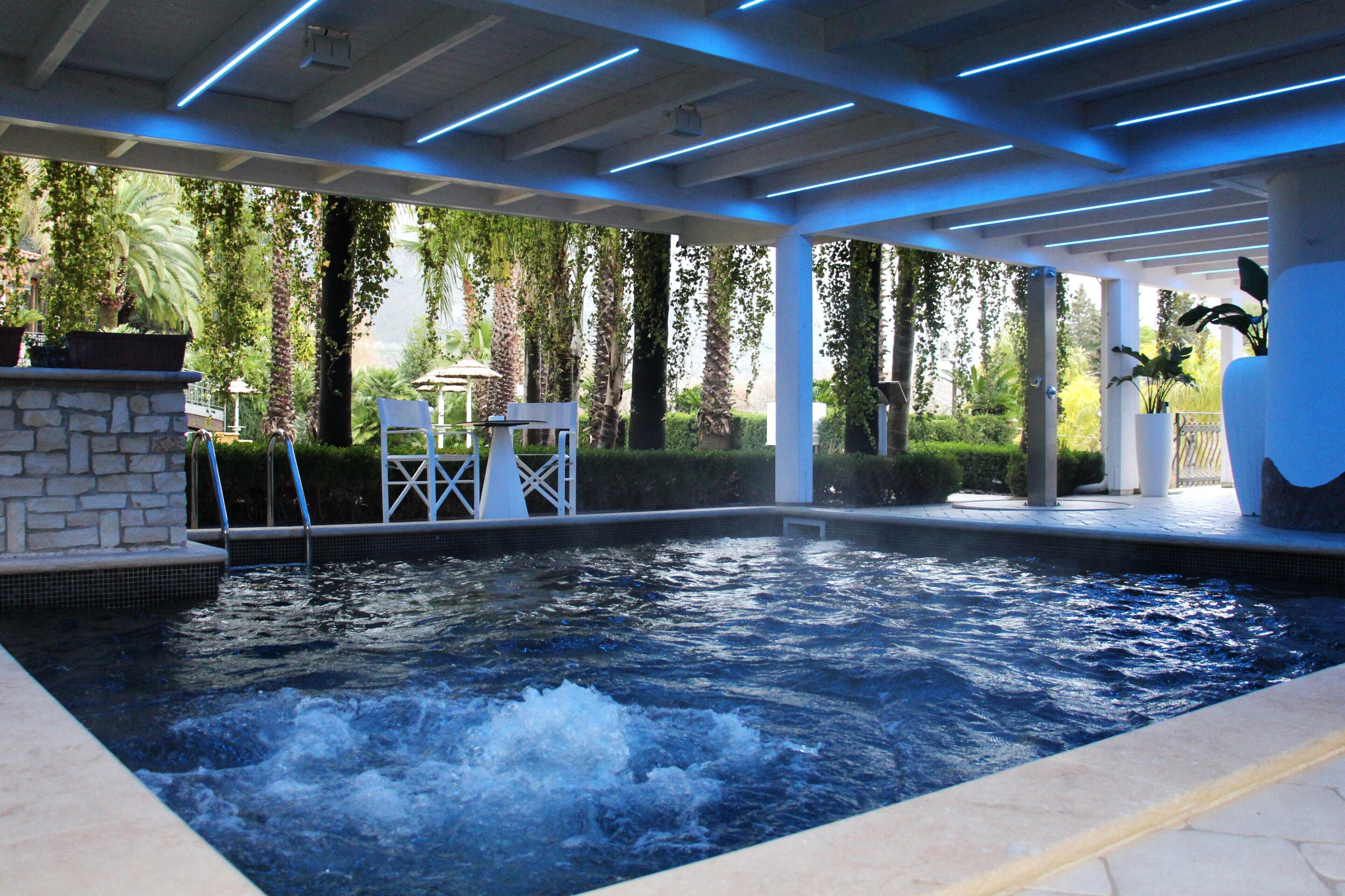 Un espace avec un jacuzzi, un mur en pierre, deux chaises et une piscine.
