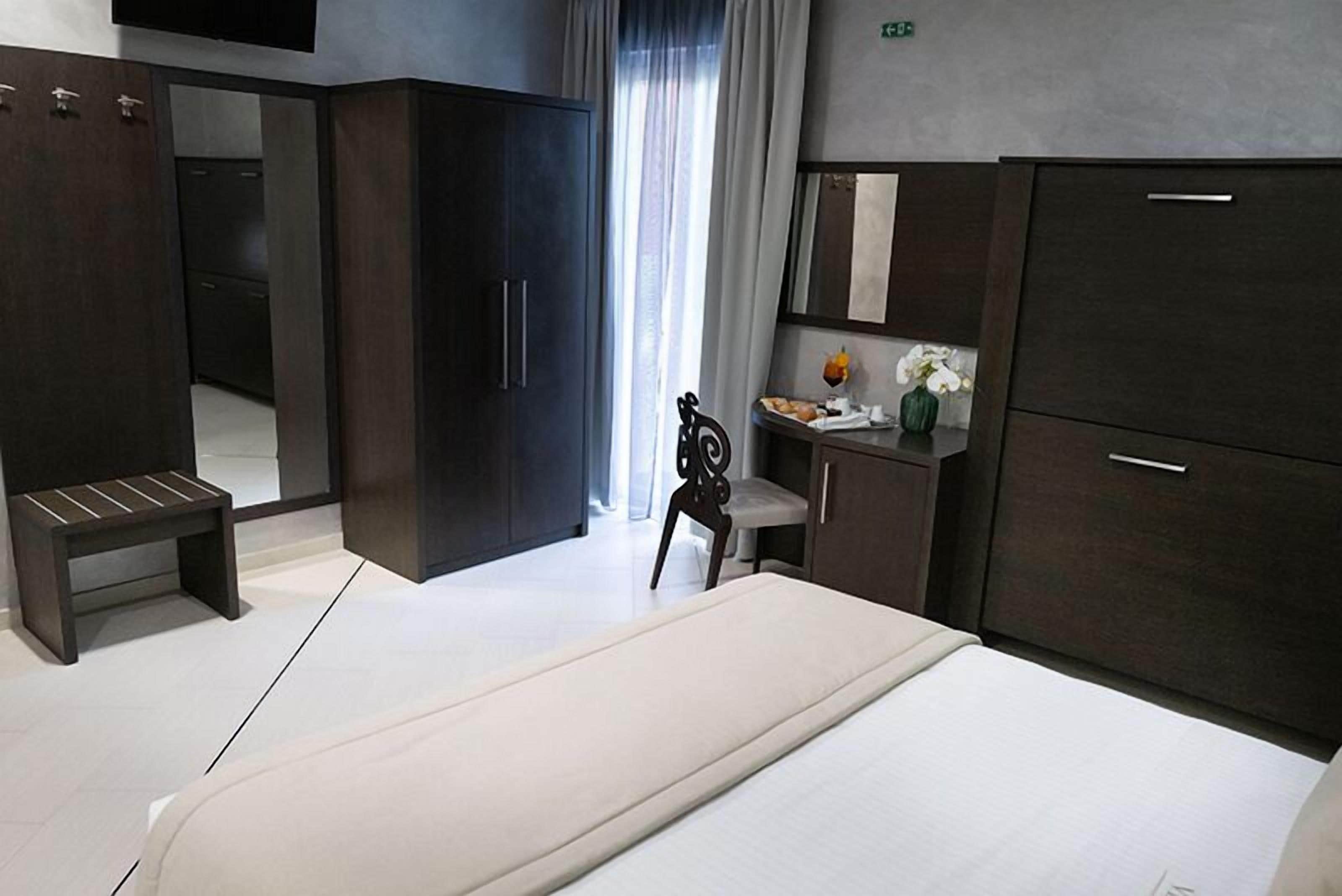 Une chambre d’hôtel moderne avec un grand lit, une armoire en bois foncé, un petit bureau avec une chaise et un banc.