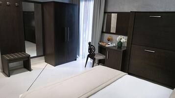 Camera d'albergo moderna con un letto grande, un'armadiatura in legno scuro, una piccola scrivania con una sedia e una panca.