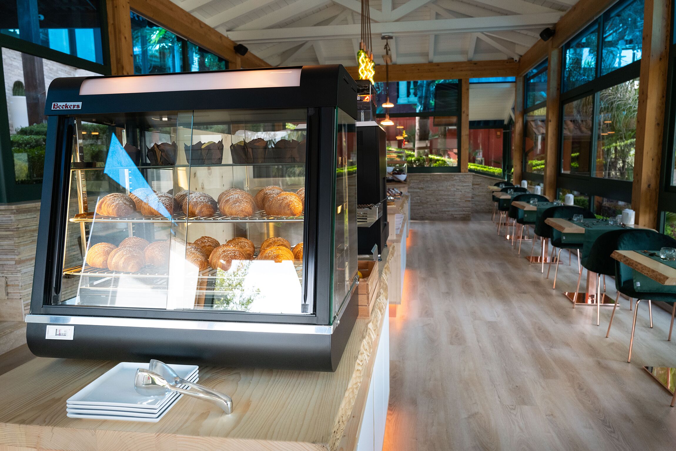 Un escaparate de pastelería con bollería, una barra de madera y una zona de estar con mesas y sillas.