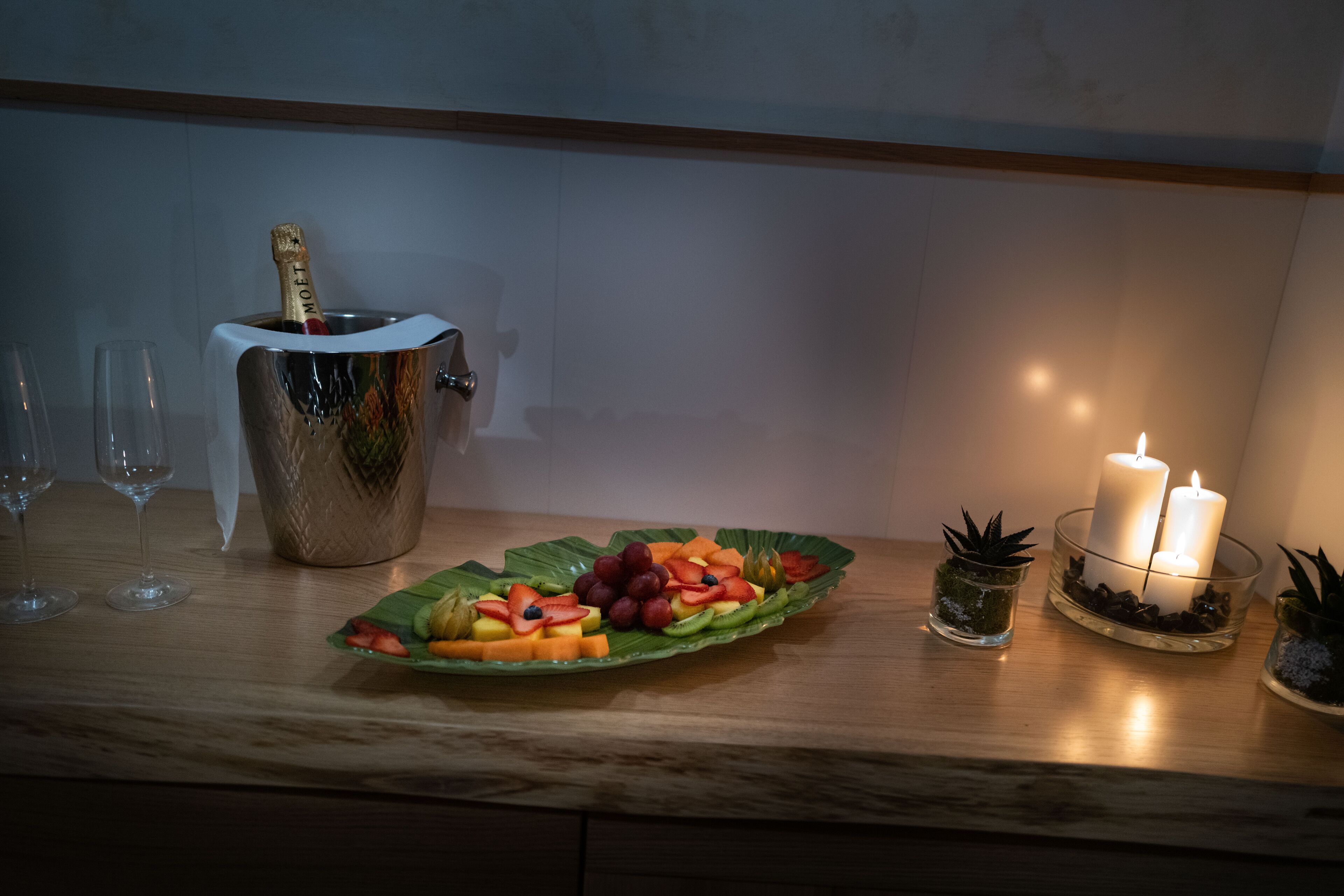 Un tavolo di legno con un vassoio di frutta, una bottiglia di champagne e delle candele.