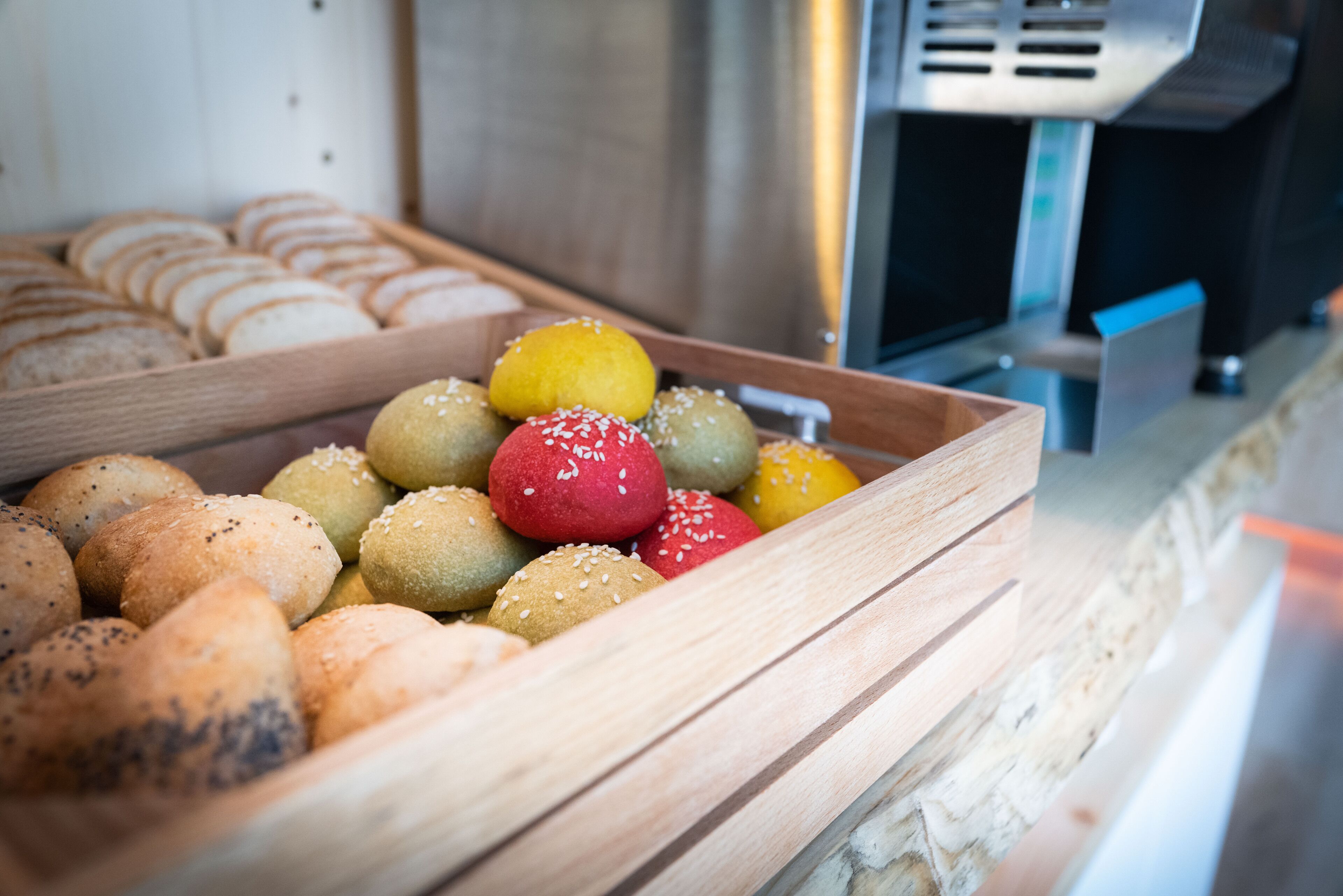 Ein Holztablett mit verschiedenen Brotsorten, darunter Brötchen und Semmeln, in einer Bäckerei.