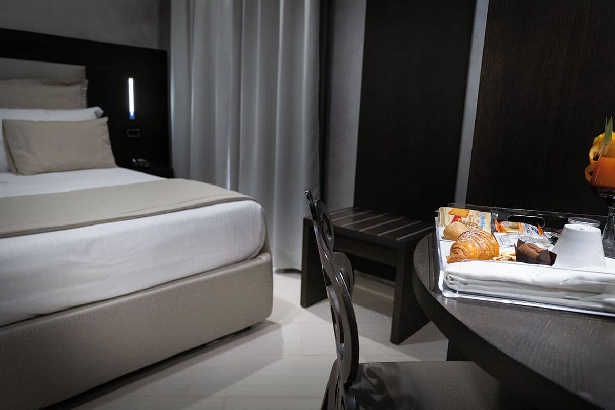 Une chambre d’hôtel avec un lit, une table de chevet sur laquelle se trouvent des articles pour le petit-déjeuner, une chaise et un mur de couleur sombre.